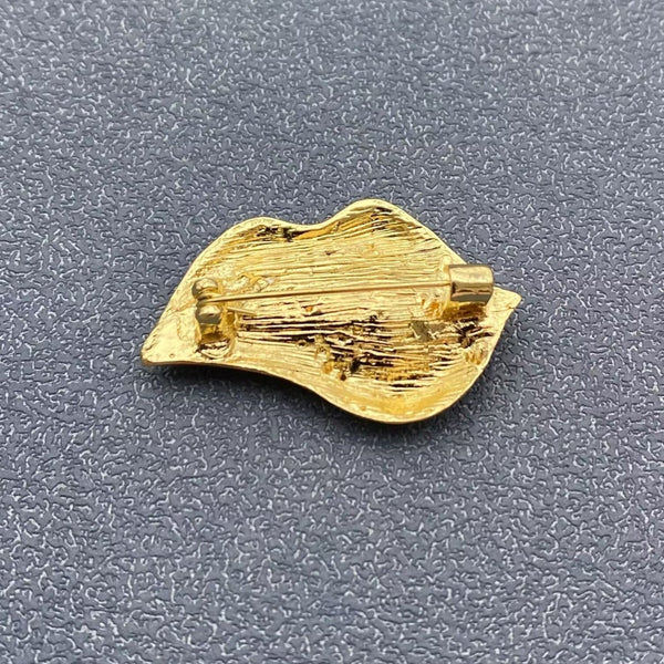 gold metal brooch of mouth with red enameled lips and white teeth in bottom lip biting pose. Shown from back