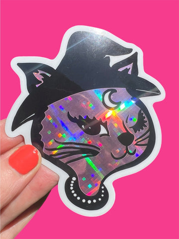 Holographic cat sticker with black witch hat held against a pink background