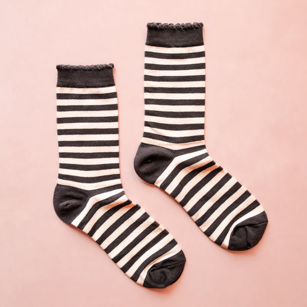 Pair of off-white crew socks with black ruffle cuff, black and white horizontal stripe, and black toes and heels; Shown flat