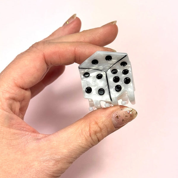 2" marbled white acetate claw style hair clip in the shape of a die with black pips. Shown on pink background held by hand