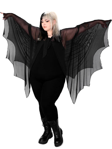 Plus size model wearing a black mesh cape with raw scalloped hemline in the shape of bat wings with sewn in arm holes and a self adjustable front tie. Shown from the front