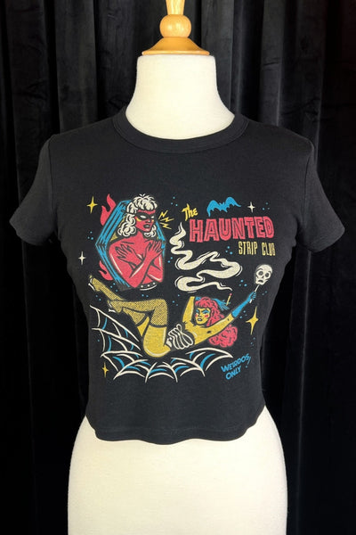 cropped black t-shirt with printed illustration of two cartoon women, one standing in a coffin wearing a mask and the other lying in a spiderweb holding a skull with the caption "THE HAUNTED STRIP CLUB" "WEIRDOS ONLY". Shown on dress form