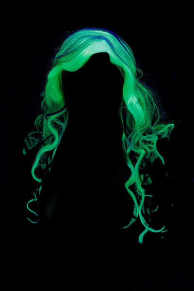 A woman wearing a long, wavy platinum white wig glowing in the dark shown charged and glowing, shown from the front