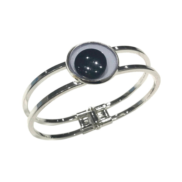 Silver metal hinged bracelet with large black and white plastic googly eye adornment on front. Shown flat