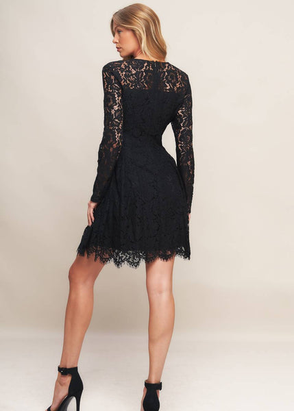 model wearing a black lace mini dress with long sleeves, round neckline with sweetheart style bodice lining, reverse yoke waistband with scalloped hem ending above the knee. Shown from back