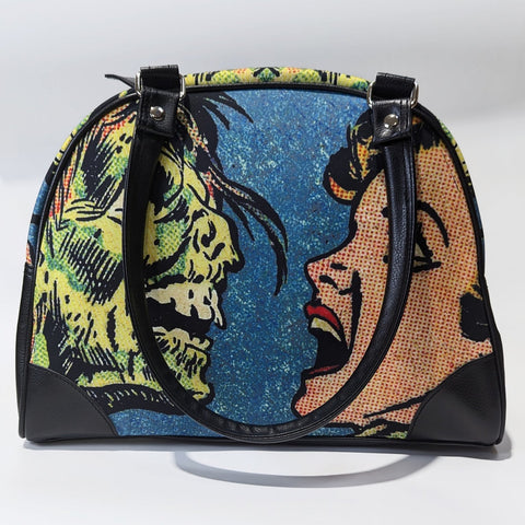 A bowler style purse with a satin body and printed image of comic book Ben Day style  art of a zombie face to face with a screaming woman. The purse has black faux leather handles, protective corners, sides, and bottom. Shown from front with handle hanging over side