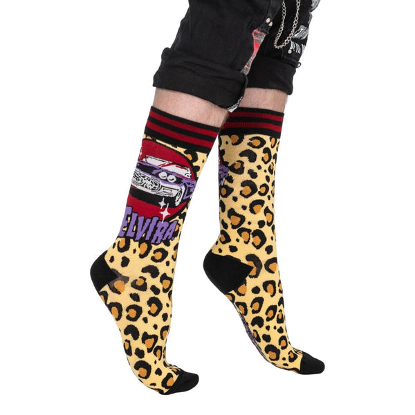 black unisex crew socks with black and red striped cuffs and black toes & heels. Outer ankle of each sock has knit-in design of Elvira's car the Macabre Mobile, a purple Thunderbird with spiderweb grille and "KICKASS" license plate above purple Elvira logo on a yellow and orange leopard print background. Shown worn by model from side