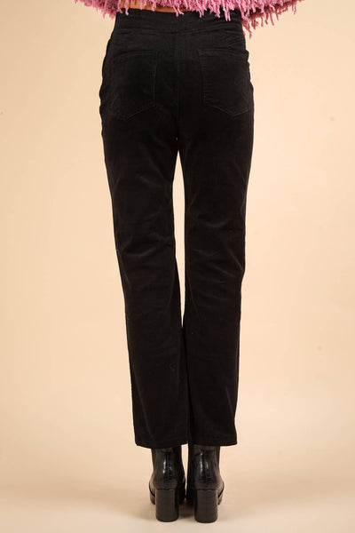 model wearing high-waisted black velvet pants with bootcut style legs, back pockets, and side zip closure. Shown from back