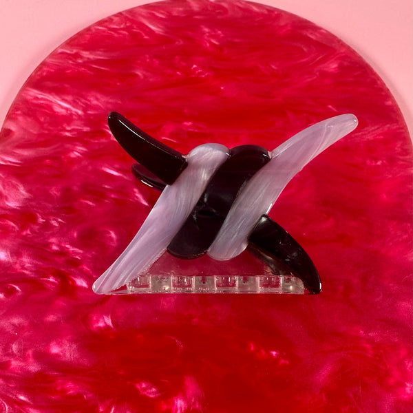 Black and grey marbled acetate hair clip in the shape of a link of barbed wire on a pink textured background