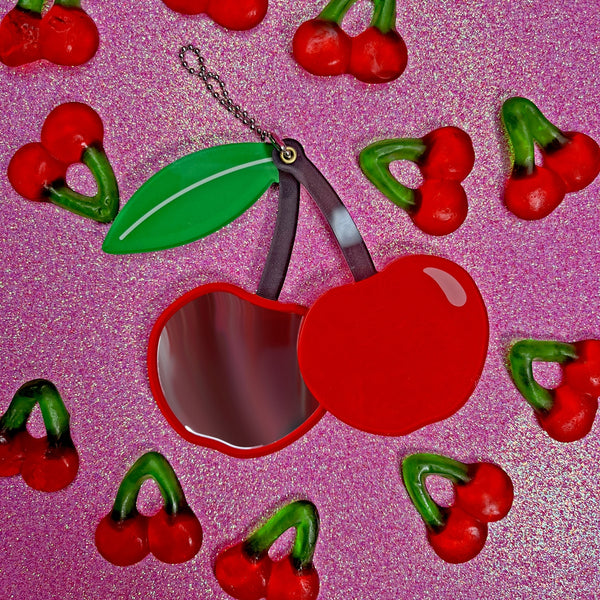 red acrylic cherry mirror with brown stem and green leaf on ball chain shown slid open on a pink sparkle background