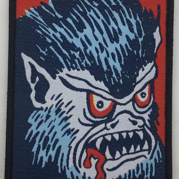 rectangular woven patch with a black embroidered border featuring a cartoony blue and red wolf with bloody mouth