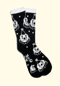 black cotton crew socks with white cuffs and an all over pattern of a white and black clown with either a smiling or frowning face. Shown flat