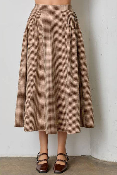 Person wearing a brown gingham patterned cream background midi skirt against a white wall.