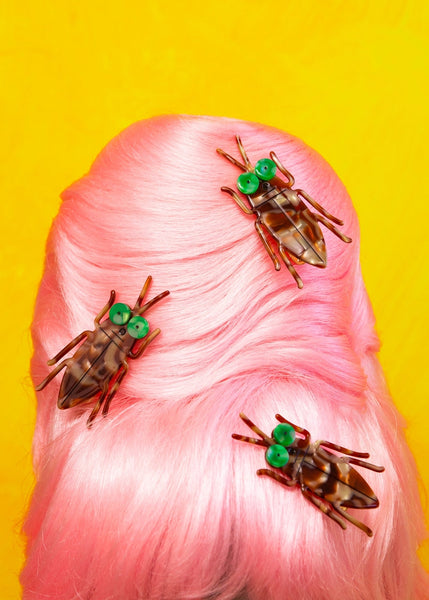 Acrylic brown swirled cockroach-shaped hair clip with large swirled green eyes. Shown in triplicate in a pink-haired beehive hairdo 