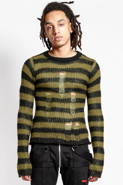 male model wearing a green and black striped long sleeve sweater with distressed detail on the front of the body on a white background