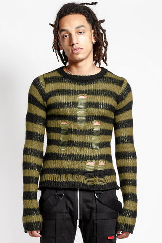 male model wearing a green and black striped long sleeve sweater with distressed detail on the front of the body on a white background