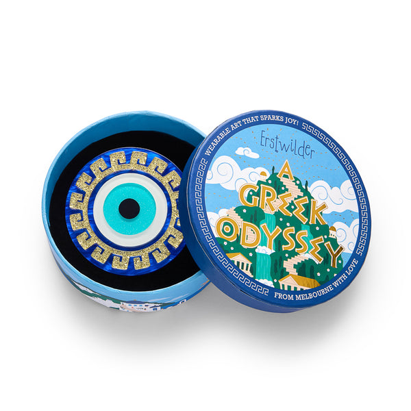 layered acrylic resin evil eye amulet brooch in blue, white, and glitter gold, shown in lllustrated round box packaging