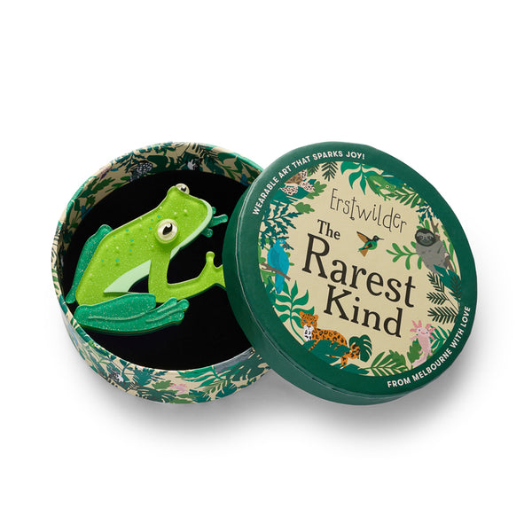 Green frog-shaped resin brooch shown in illustrated round box packaging