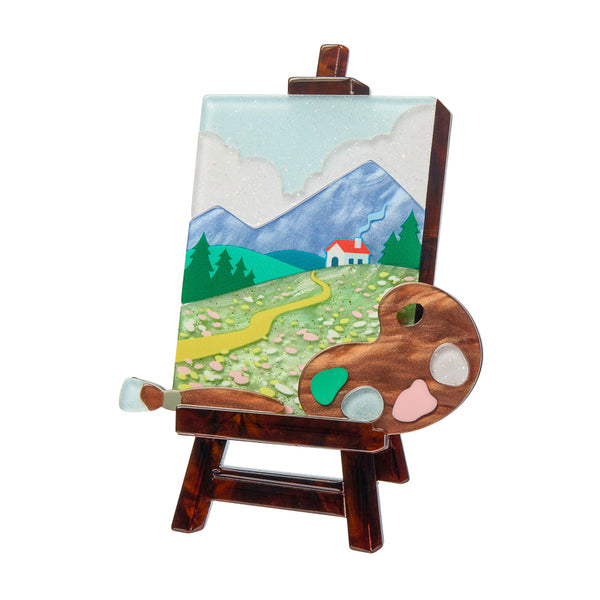 layered acrylic resin brooch depicting a landscape painting on an easel with palette and paintbrush