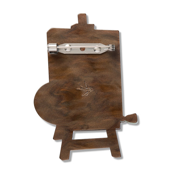 solid brown back layer of layered acrylic resin brooch depicting a landscape painting on an easel with palette and paintbrush