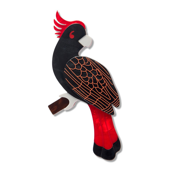 black, red, and white cockatoo perched on a branch acrylic resin brooch, shown against a plain white background.