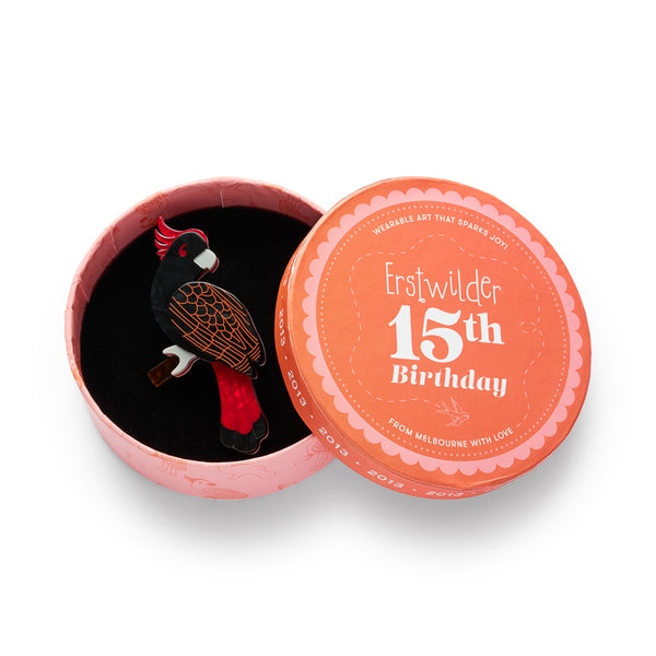 black, red, and white cockatoo perched on a branch acrylic resin brooch, shown in illustrated round box packaging