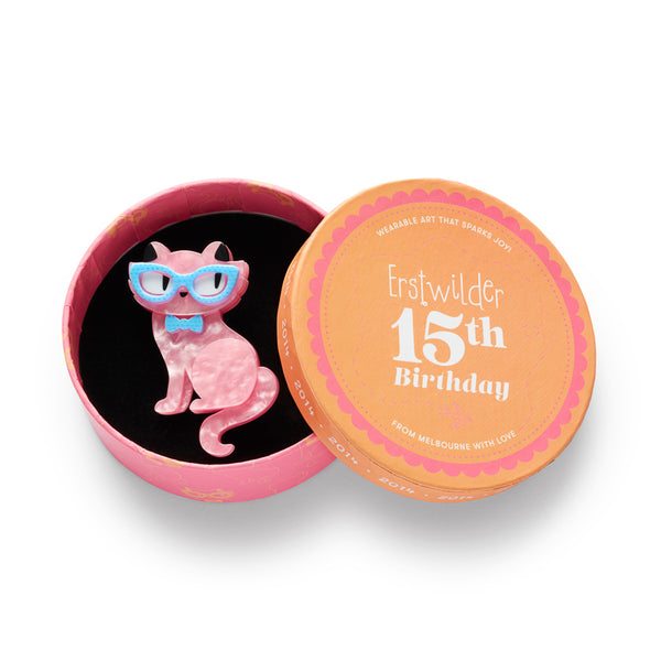 acrylic resin brooch of a pink cat wearing blue glasses and bow tie, shown in illustrated round box packaging