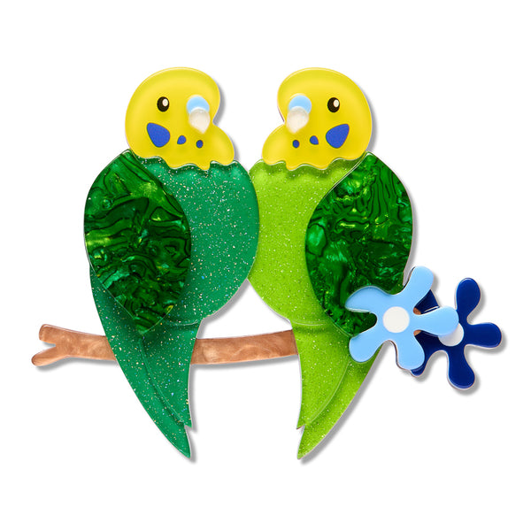 acrylic resin brooch of two stylized green birds with yellow heads perched on a brown branch, with blue flower accents, shown on a plain white background.