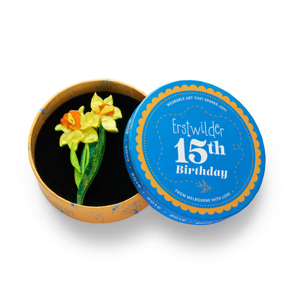 acrylic resin brooch depicting two yellow daffodils with orange centers and green leaves, shown in illustrated round box packaging