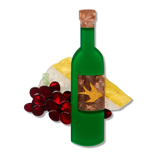 acrylic resin brooch of a green wine bottle with a cork stopper and a decorative label featuring a gold swallow on a brown background, styled with red grapes and a cheese wedge on a white background.