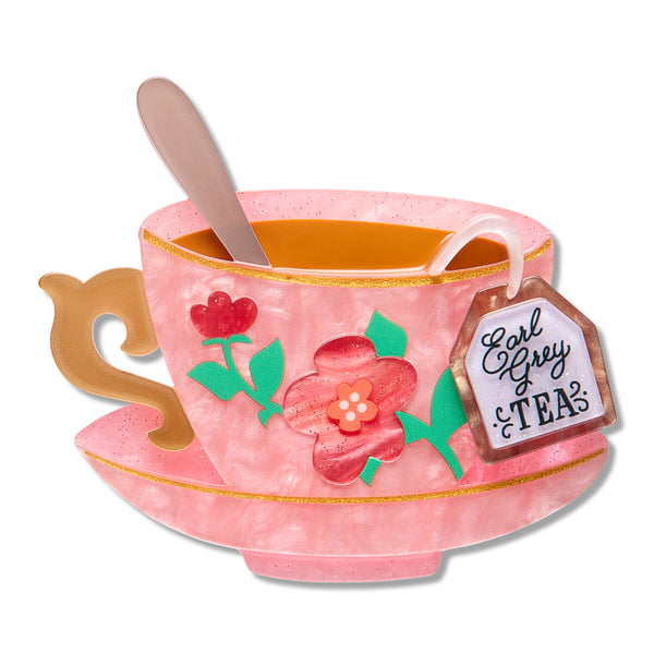A marbled pink resin teacup and saucer set brooch with gold rim, floral decoration, a spoon inside, and a hanging tea tag reading 'Earl Grey TEA'.