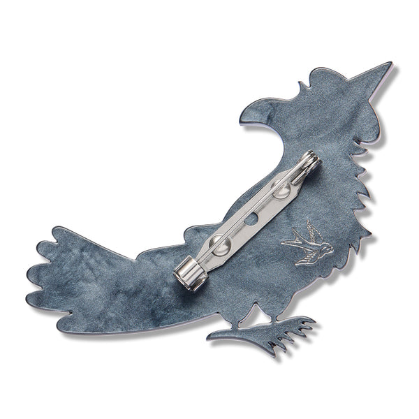 back view of raven-shaped brooch with a textured slate-blue enamel body and a silver-tone metal pin mechanism on the back, shown against a plain white background.