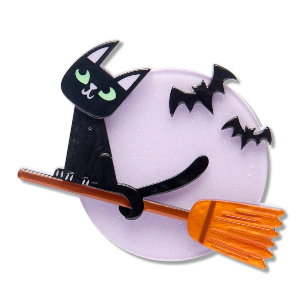 A Halloween-themed layered acrylic resin brooch featuring a black cat with green eyes sitting on an orange broomstick in front of a glittery light purple full moon, with two black bats flying above, all on a white background.