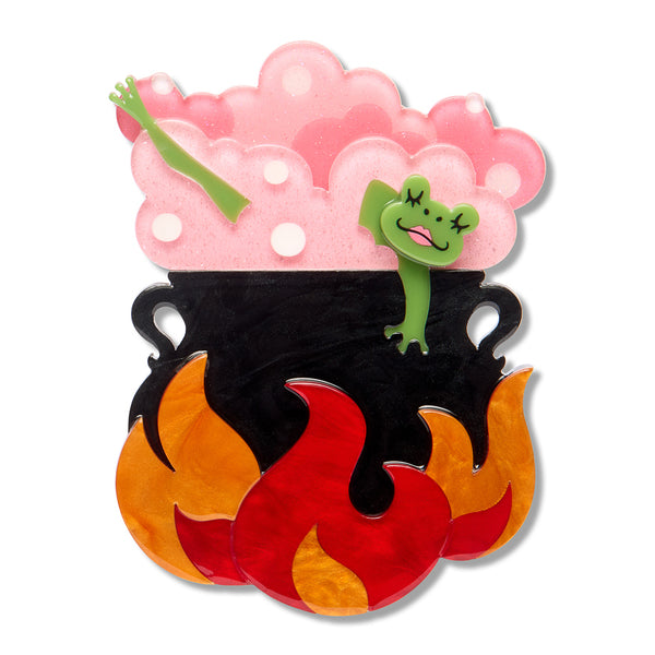 A layered acrylic resin brooch shaped like a black cauldron with orange and red flames at the bottom, pink bubbly steam at the top, and a small green frog bathing inside. The piece is shown on a plain white background with a soft drop shadow.