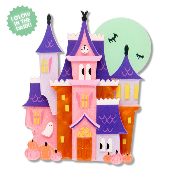 A colorful Halloween haunted house acrylic resin brooch with pink, purple, orange, and white sections, plus pumpkins, bats, a ghost, and a green starburst that says 'I GLOW IN THE DARK!'.