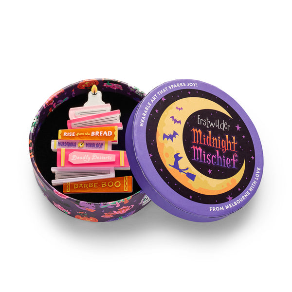A book stack-shaped acrylic resin brooch featuring book spines in pink, orange, yellow, and white with text reading 'RISE from the BREAD', 'MURDEROUS MIXOLOGY', 'Deadly Desserts', and 'BARBE-BOO'. Shown in illustrated round gift box packaging. 