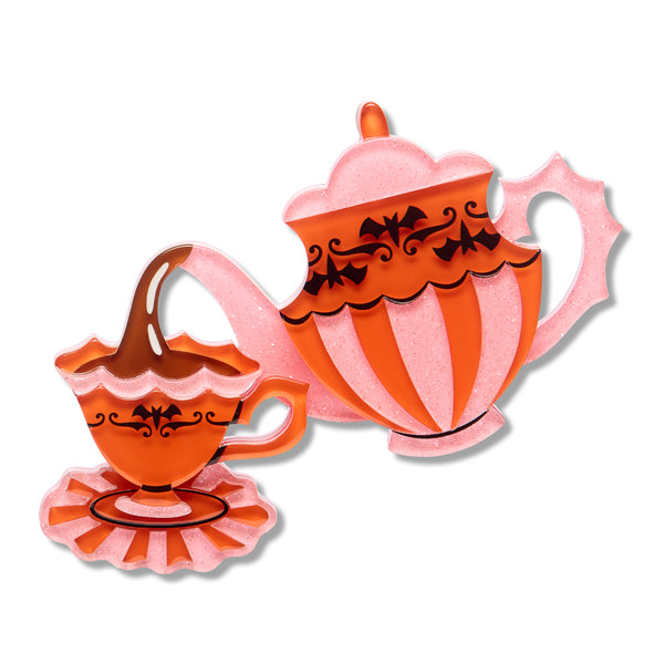A pink and orange glittery teapot and matching teacup with black decorative scrollwork and bats acrylic resin brooch, shown on a plain white background.