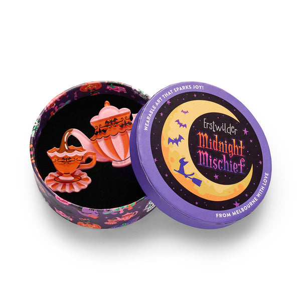 A pink and orange glittery teapot and matching teacup with black decorative scrollwork and bats acrylic resin brooch. Shown in illustrated round gift box packaging.