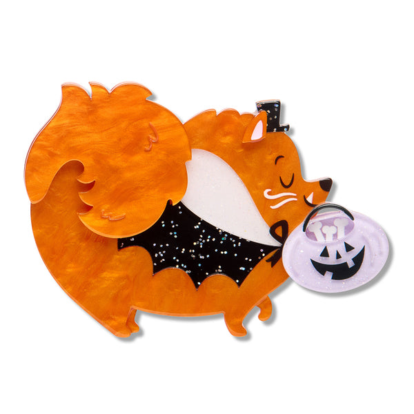 acrylic resin brooch depicting the side view of a fluffy orange dog wearing a glitter black cape and top hat, and carrying a jack-o-lantern candy bucket filled with bones in its mouth
