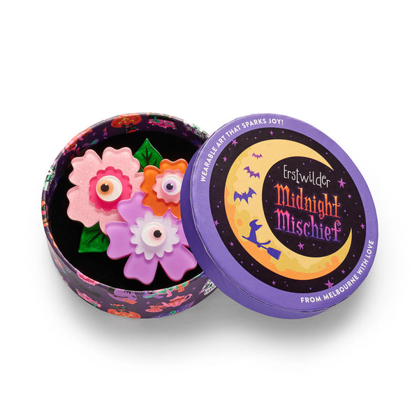 Acrylic resin brooch depicting three colorful flowers with eyeball centers, shown in illustrated round box packaging