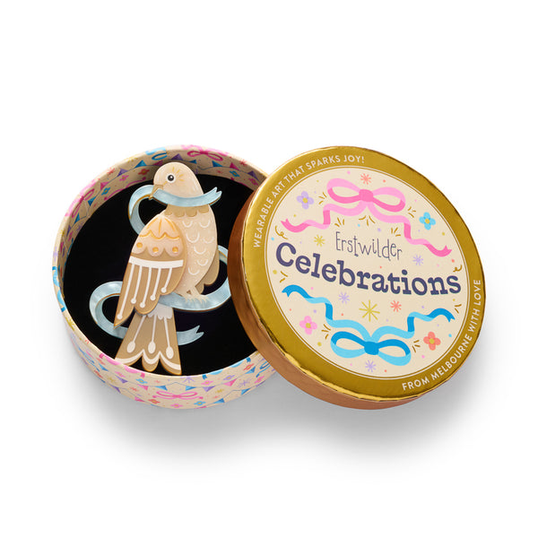 dove acrylic resin brooch in warm beige and tan tones with white patterned details, a light blue ribbon around its neck, and a small black eye. Shown in illustrated round gift box packaging.