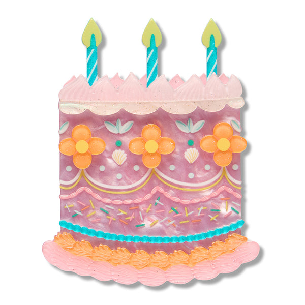 cake-shaped acrylic resin brooch with pink frosting, orange flowers, teal candles, and multicolor sprinkles on a white background.