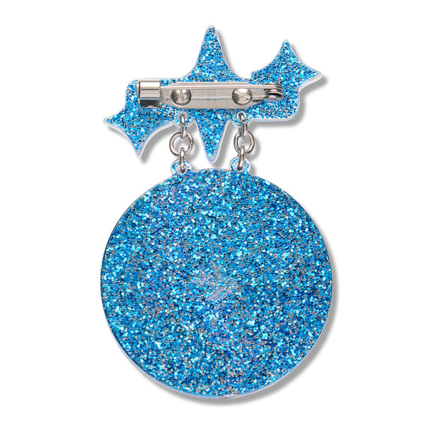 A blue glitter acrylic resin back layer of a circular disc dangling from two dangling star-shaped elements connected by silver-toned metal rings and a pin clasp at the top, shown on a plain white background.