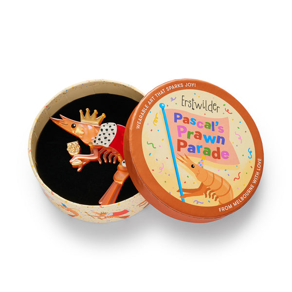 A stylized shrimp layered acrylic resin brooch with a gold crown, red body, white-and-black spotted trim, and a small gold cup, shown in illustrated roun box packaging