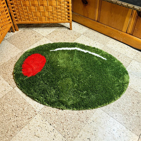 An oval rug made to look like a pimento stuffed green olive with a white highlight detail. Shown laid on a linoleum floor