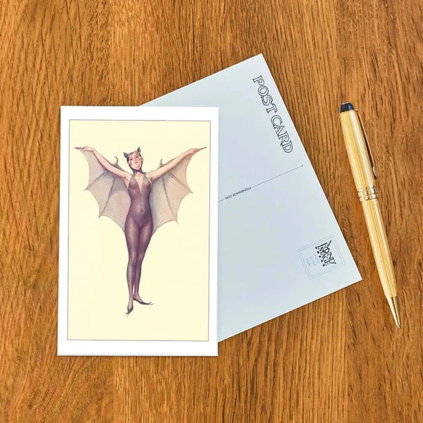 Postcard with a bat-themed design on a wooden surface with a pen.