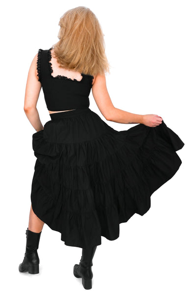 Model wearing a black cotton poplin midi skirt with an elastic waistband and four tiered ruffled layers with side seam pockets. Shown from back