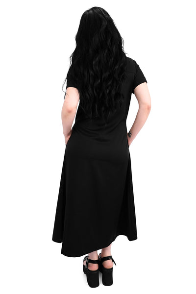Model wearing a black rayon blend button-front slightly relaxed fit dress with a pointed collar, cuffed short sleeves, slightly a-line midi length skirt, and side seam pockets. Shown from back with hands in pockets
