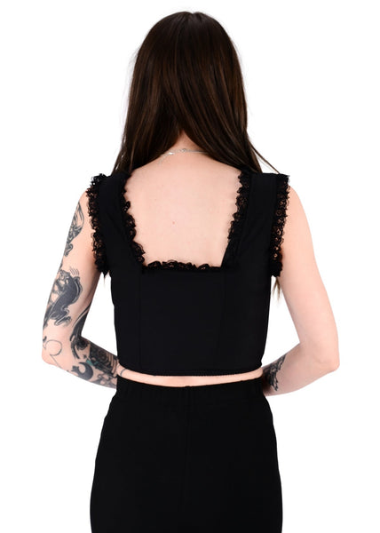 model wearing black cotton twill corset top with metal hook and eye fasteners down length of bodice, flexible boning, and scoop neck with black floral lace trim. Shown from back