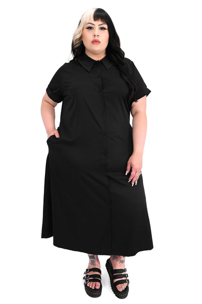 Plus size model wearing a black rayon blend button-front slightly relaxed fit dress with a pointed collar, cuffed short sleeves, slightly a-line midi length skirt, and side seam pockets. Shown from front